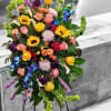 Tall multicolored standing spray with sunflowers, roses, orchids, and other blooms on a metal easel