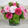 Compact arrangement of pink roses, white lisianthus, and green dianthus in a clear glass cube vase