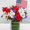 Red, white, and purple floral arrangement in a glass vase with an American flag