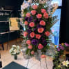 A graceful standing tribute featuring premium pink and purple roses, lush tropical