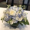 White roses and pale blue hydrangeas in a square glass vase