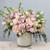 Large pastel pink and white flower arrangement with roses, orchids, and tulips in a white cylinder vase