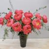Tall arrangement of bright pink peonies with trailing eucalyptus in a textured glass vase