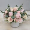 Low arrangement of pale pink roses and spray roses with eucalyptus in a white ceramic vase