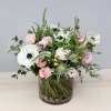Pastel pink roses and white anemones arranged in a glass cylinder vase with stones.