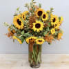 Tall glass vase of yellow sunflowers with orange filler blooms and variegated foliage