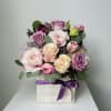 Pink and lavender roses arranged in a square box with a purple ribbon