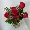 Red roses arranged in a clear glass vase with greenery and small accent flowers