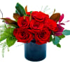Red roses arranged in a dark blue vase with mixed greenery