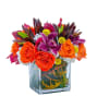 Bright bouquet of orange roses and purple flowers in a glass vase