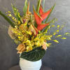 Tropical arrangement with red heliconia, yellow orchids, and peach roses in a white vase