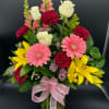 Mixed bouquet with pink gerbera daisies, yellow lilies, white roses, and red carnations in a vase with a pink bow.