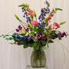 Tall mixed bouquet with lilies, roses, and purple blooms in a glass vase