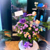 Purple and peach flower arrangement with a Happy Birthday sign in a black container