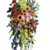Tall standing floral spray with roses, lilies, sunflowers, and blue accents