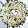 White floral wreath on a black easel with lilies and roses
