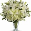 White lilies and mixed white flowers in a clear glass vase