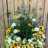Large standing floral spray with sunflowers, white carnations, and blue flowers