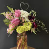 Mixed bouquet of pink roses, white daisies, and dark orchids in a glass vase