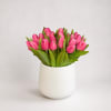 Thirty bright pink tulips arranged in a clean white ceramic vase make