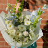 Bouquet of white and pale blue flowers wrapped in white paper with a blue ribbon