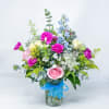 Mixed bouquet of pink, blue, and white flowers in a glass vase with a blue ribbon