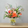 Bouquet of orange roses and pastel flowers in a glass vase with a yellow ribbon