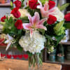Vase arrangement of red roses, pink lilies, and white hydrangeas in a clear glass cylinder