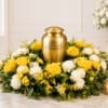 Yellow roses and white mums surround a gold urn with candles nearby