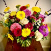 Bright mixed bouquet of yellow gerbera daisies, red roses, and assorted blooms in a clear glass vase