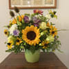Mixed arrangement with sunflowers, yellow daisies, roses and purple blooms in a green ceramic vase