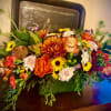 Low centerpiece of orange roses with yellow and white mums in a green rectangular vase