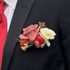Pink, red, and cream rose boutonniere on a dark suit jacket