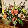 Low compote arrangement of peach roses, yellow daisies, and mixed flowers on a wooden table.