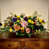 Low rectangular arrangement of mixed yellow, pink, orange, and purple flowers on a wooden dresser