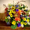 Colorful fall cornucopia arrangement with yellow sunflowers, orange roses, and mixed blooms in a woven horn basket