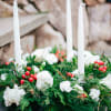 Evergreen candle ring with white flowers, red berries, and three white taper candles