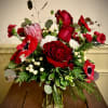 Red and white floral arrangement with roses, anemones, and evergreens in a glass vase on a wooden table.