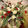 Rustic arrangement of white roses and red carnations with winter greenery in a metal container on a wood slice.