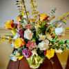 Mixed arrangement of yellow and white roses with pink carnations in a clear glass vase on a wooden table.