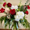 Tall arrangement of red roses, red carnations, white hydrangeas and evergreen foliage in a clear glass vase