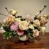 Low arrangement of cream roses, pink mums, and ranunculus in a white ceramic bowl