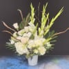 Tall white floral arrangement in a white vase with green accents