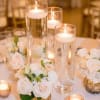 White rose centerpieces with tall glass candles on a table
