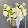Large arrangement of white roses and hydrangeas with green accents in a silver hatbox container.