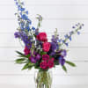 Mixed bouquet of pink roses and blue-purple flowers in a clear glass vase
