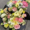 Mixed bouquet of pink, yellow, and white flowers wrapped in black paper