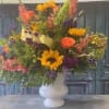 Mixed bouquet in a white vase with sunflowers, roses, and purple blooms