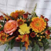 Autumn floral arrangement with orange and yellow blooms in a low container