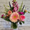 Mixed pink and peach flowers in a glass jar vase with a ribbon